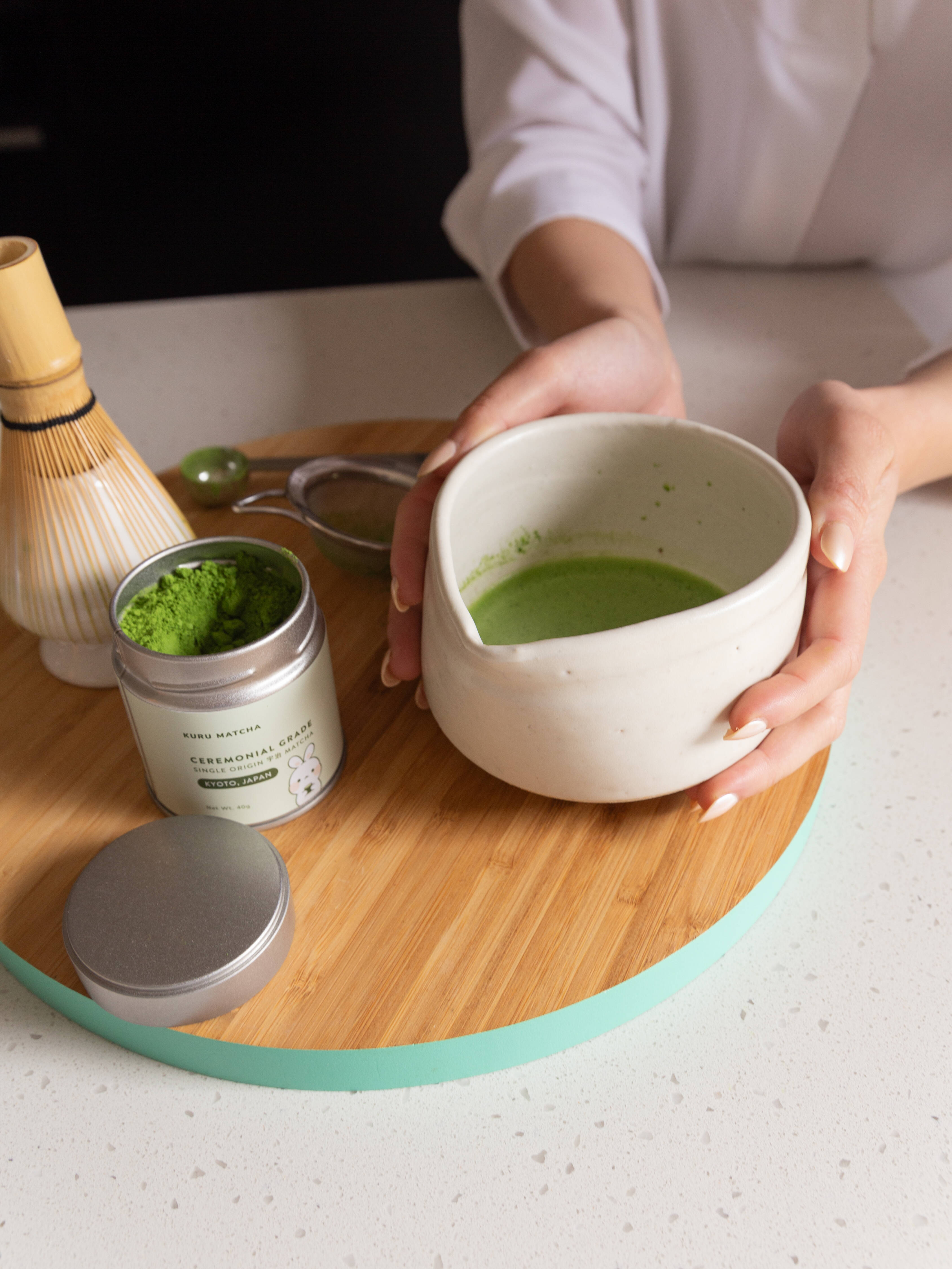 Person holding a chawan bowl filled with freshly prepared matcha, made with traditional matcha whisk and tools